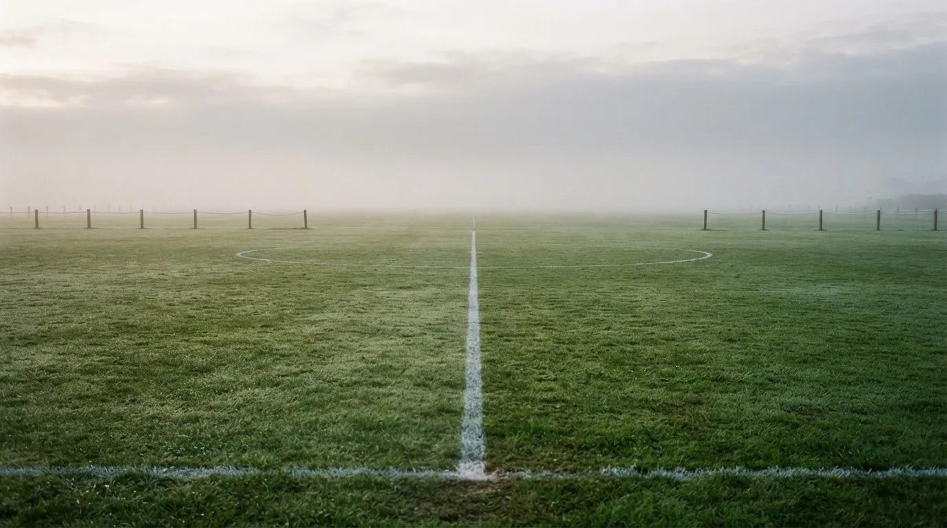 Ein leeres Fußballfeld im Morgennebel, die Mittellinie verliert sich im Dunst, kein Mensch ist zu sehen.