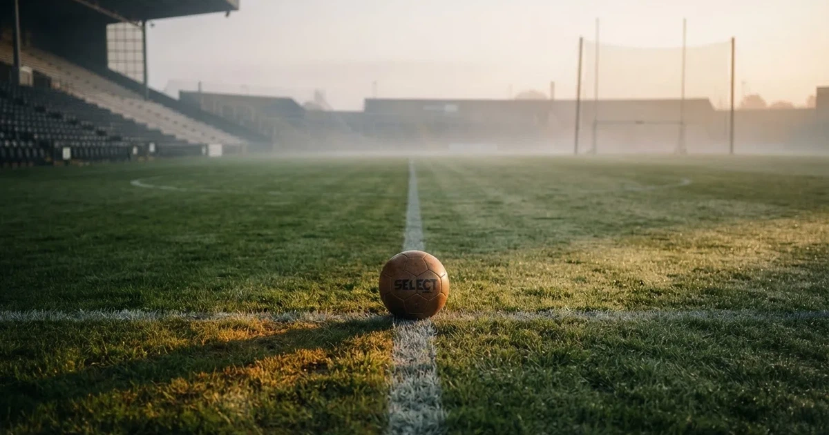 Ein Fußball liegt auf der Mittellinie eines leeren Rasenplatzes, die Kreidelinie verläuft scharf durchs Bild im Morgenlicht.